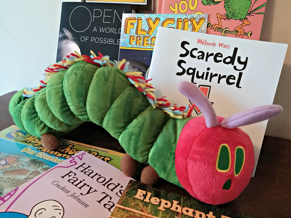 Stuffed "hungry catterpillar" lying in front of books 