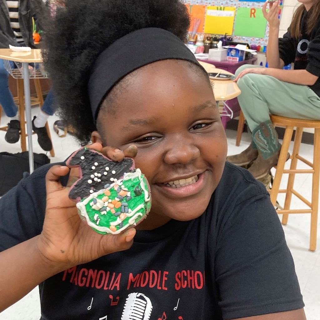 Denicia Todd holds up her witch cookie while in the background other students are eating.