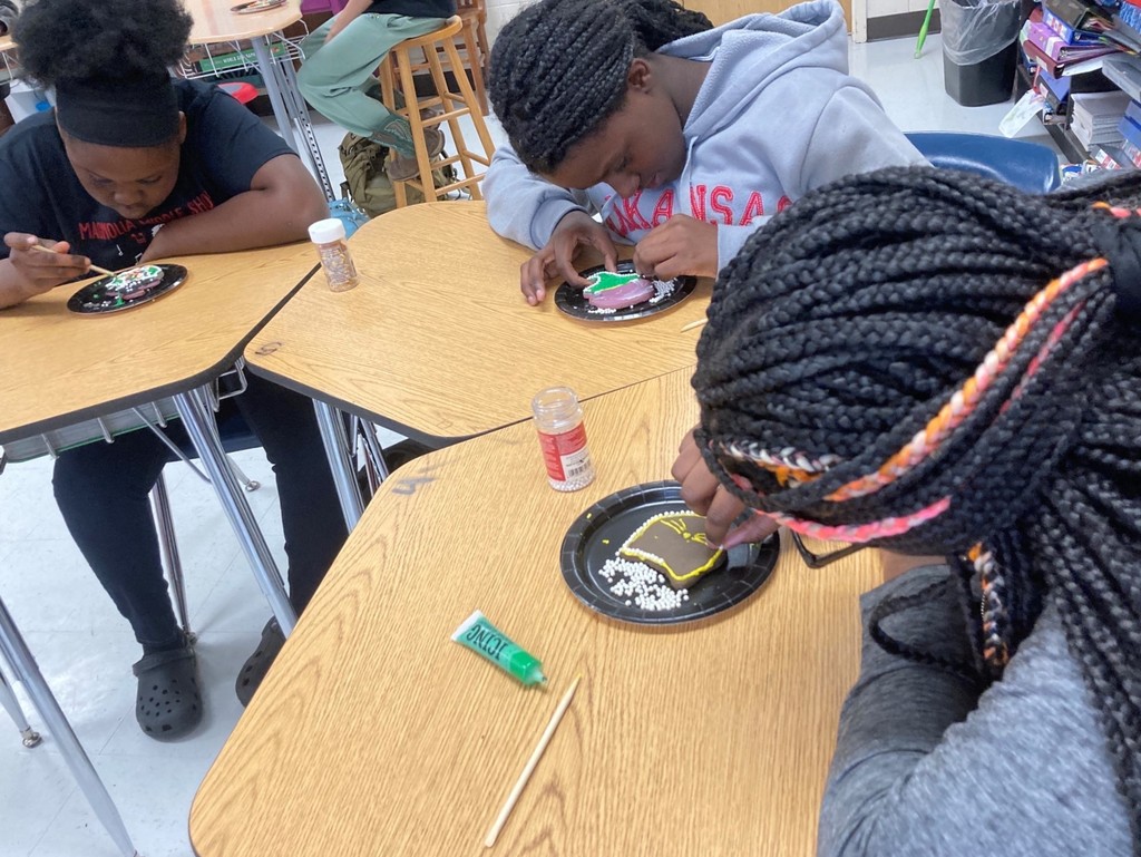 Denicia Todd, La'Miya Hughey, and A'Ziyah Stringer work on their cookies. A'Ziyah and LaMiya are applying sprinkles while Denicia uses a skewer to move her icing.