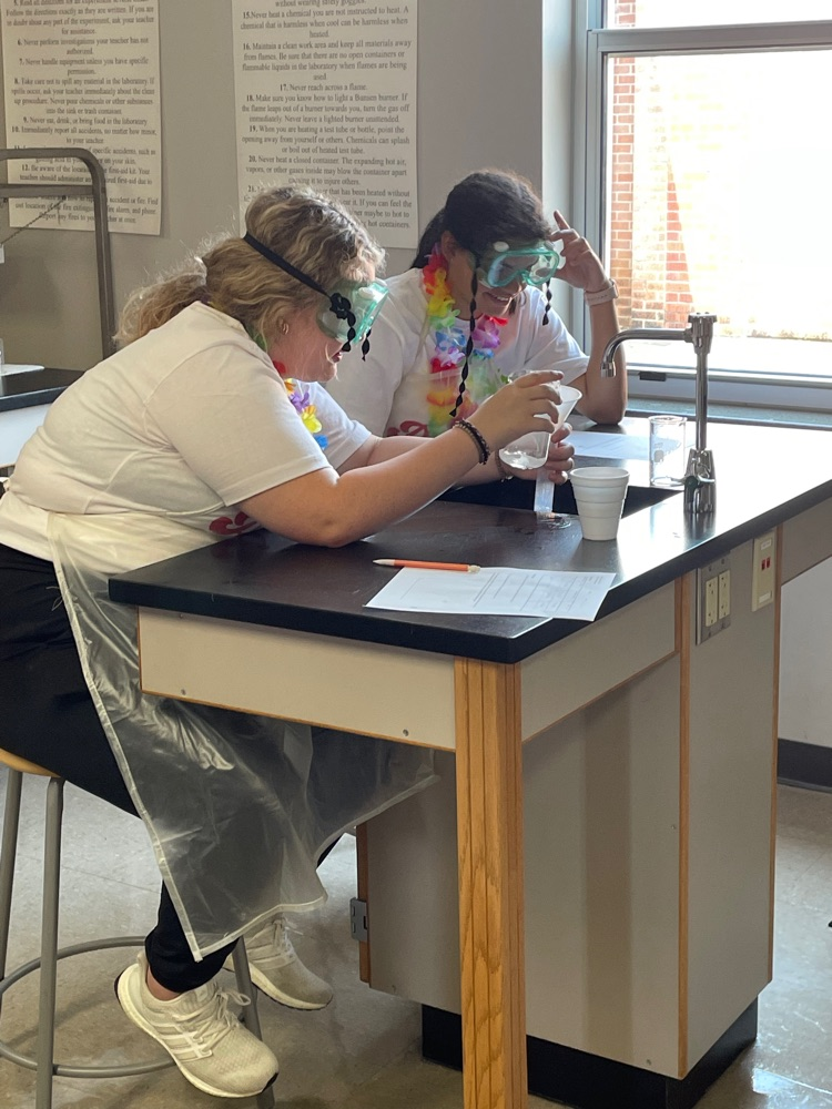 2 students pouring solution from a beaker to a graduated cylindee